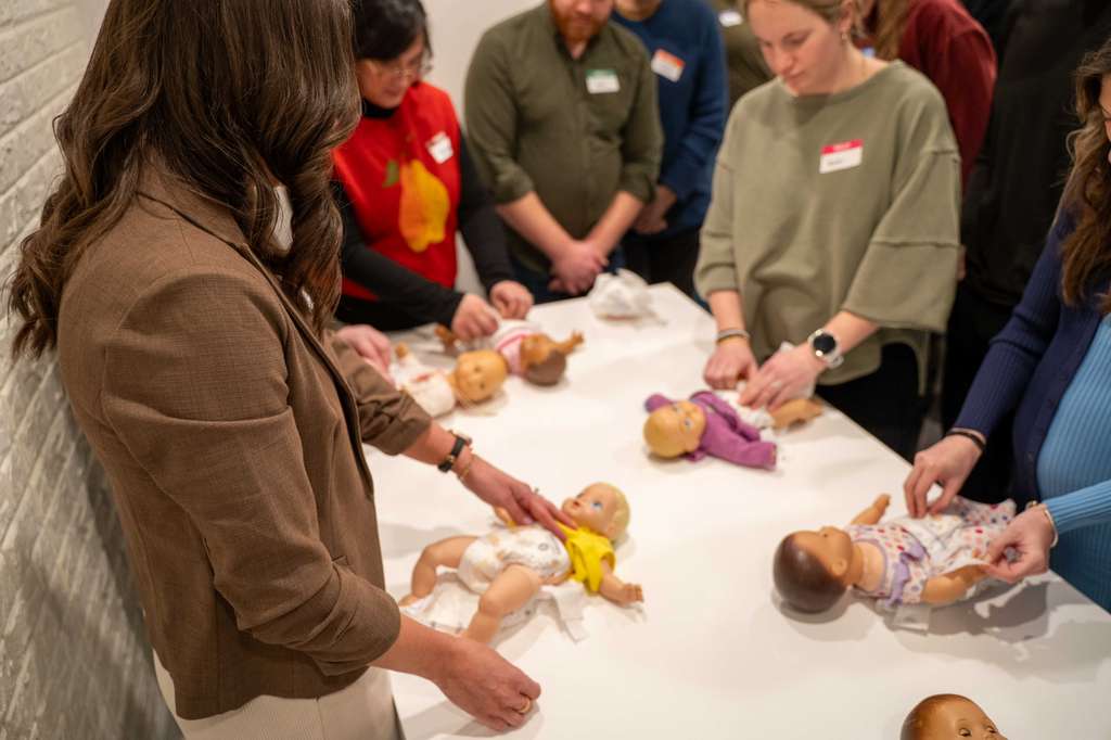 Expecting parents practicing diapering techniques on infant dolls during a prenatal education workshop.